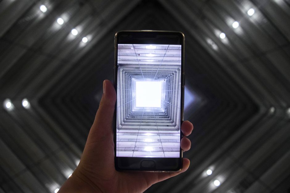 Smartphone ekran prikazuje simetrično osvijetljen interijer zgrade koji ističe modernu tehnologiju.