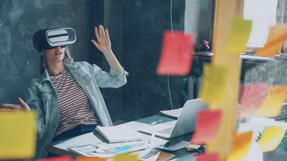 Članica tima koristi VR headset dok razmišlja o idejama za projekt s ljepljivim papirićima i laptopom